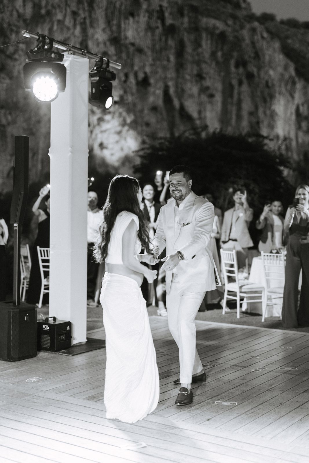 First dance at night under the lit cliff of Lake Vouliagmeni, black and white