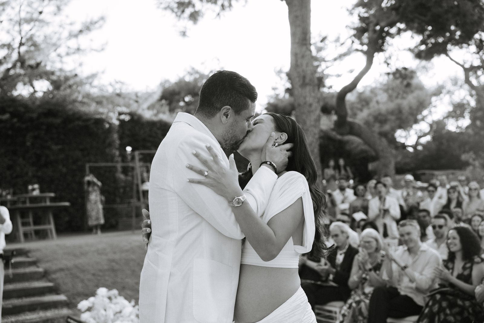 First kiss as guests cheer at the Lake Vouliagmeni ceremony, black and white